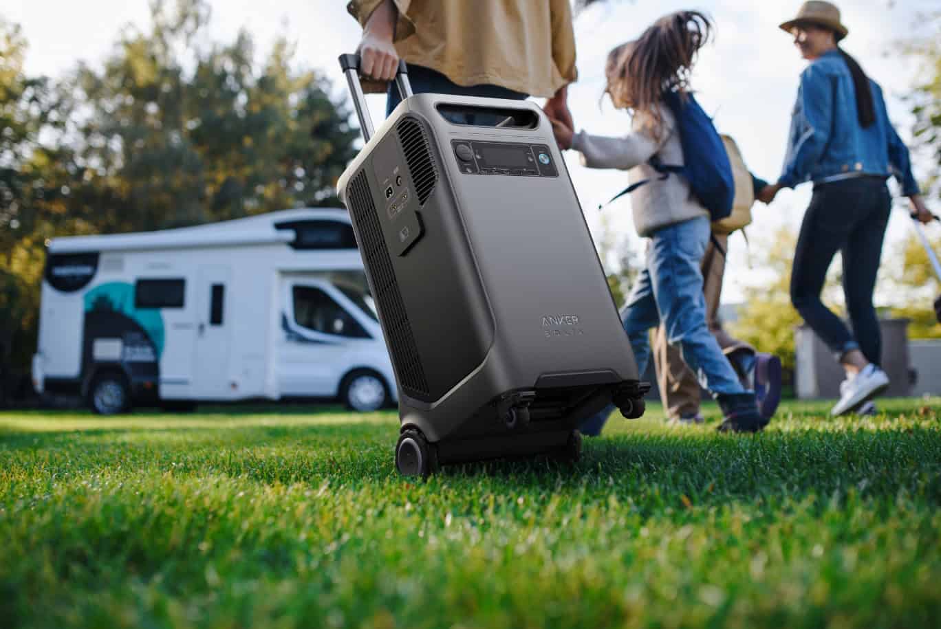 Family on grass beside camper van using portable Anker power station with wheels
