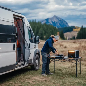 Man cooking outdoors beside van using Anker power station on folding table
