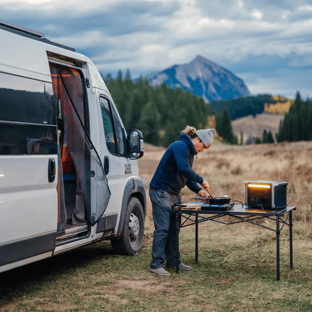 Man cooking outdoors beside van using Anker power station on folding table